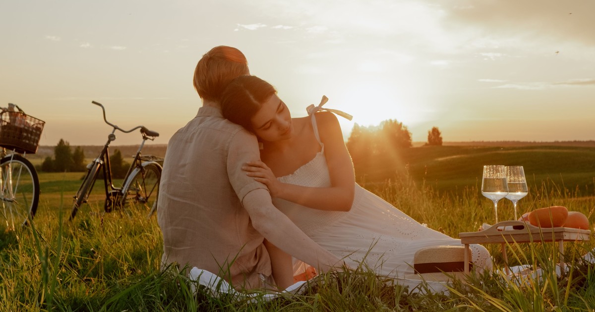 "Couple embracing at sunset in a grassy field during a romantic picnic date"